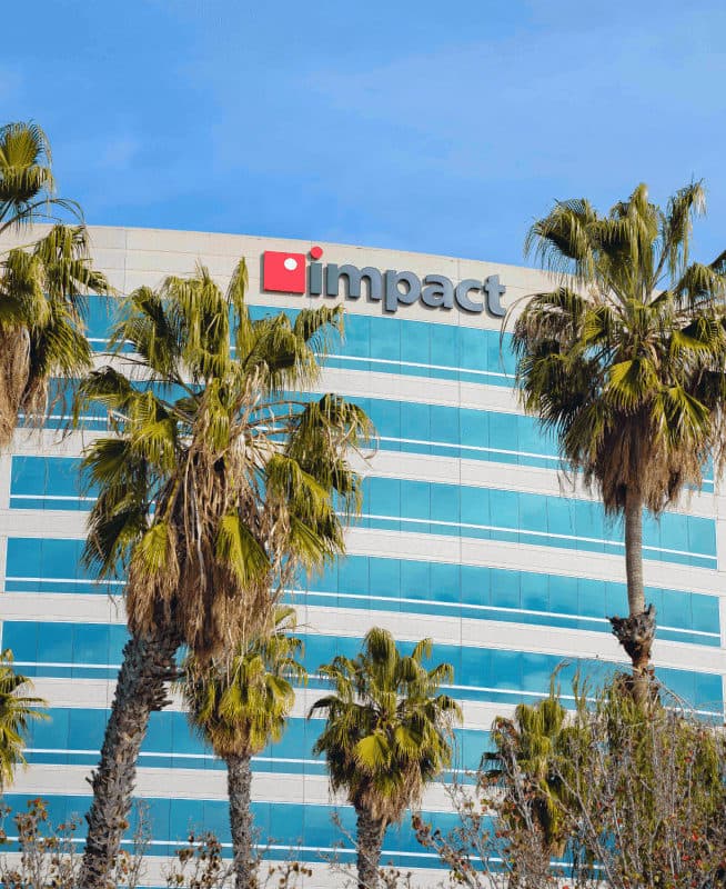 Multi-story building in Anaheim with palm trees in front of it, framing the Impact Networking logo on top of the building