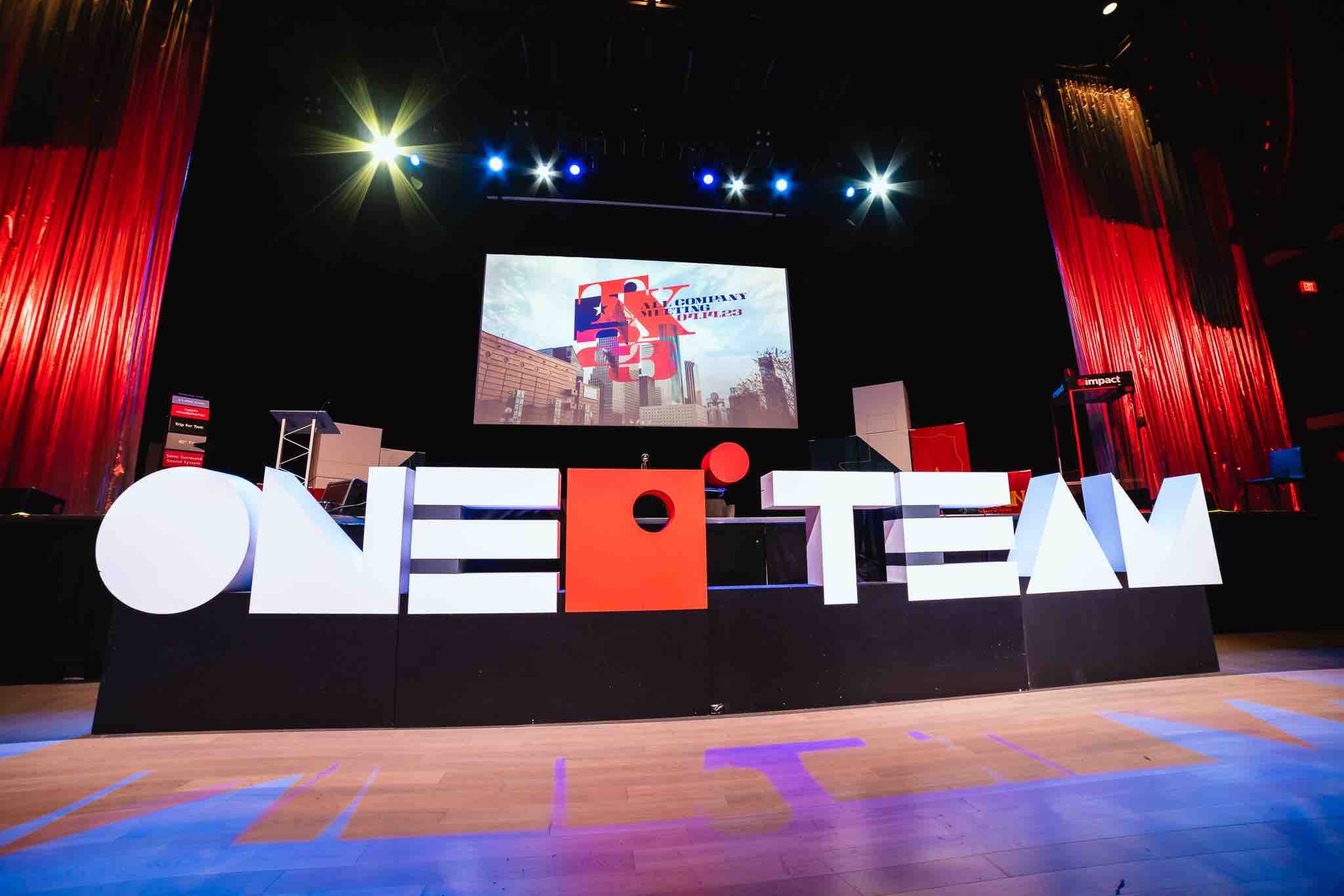 a stage with red curtains on each side and foam letters in front spelling "One Team"