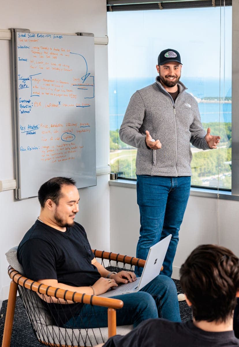 A group of people working in the corner of a relaxed office surrounded by windows