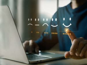 A person sitting at a desk with a laptop in front. Floating on the image is a scale of smiley faces ranging from a frowny face to a happy face with corresponding star ratings underneath ranging from 1 to 5