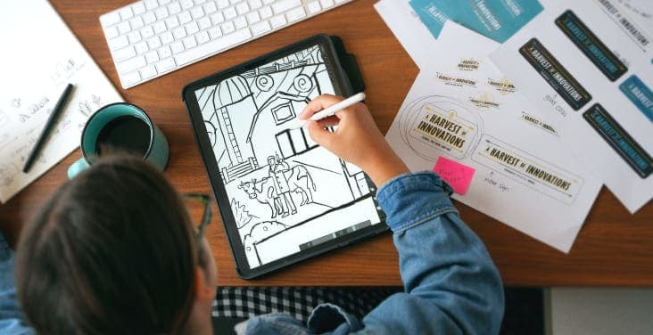 An art director working at a desk, drawing a doctor in a farm scene on a tablet.
