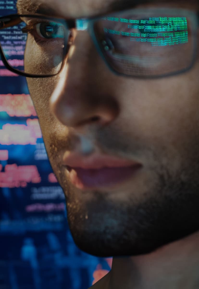 man with glasses looking at screen with green code reflected in his lenses