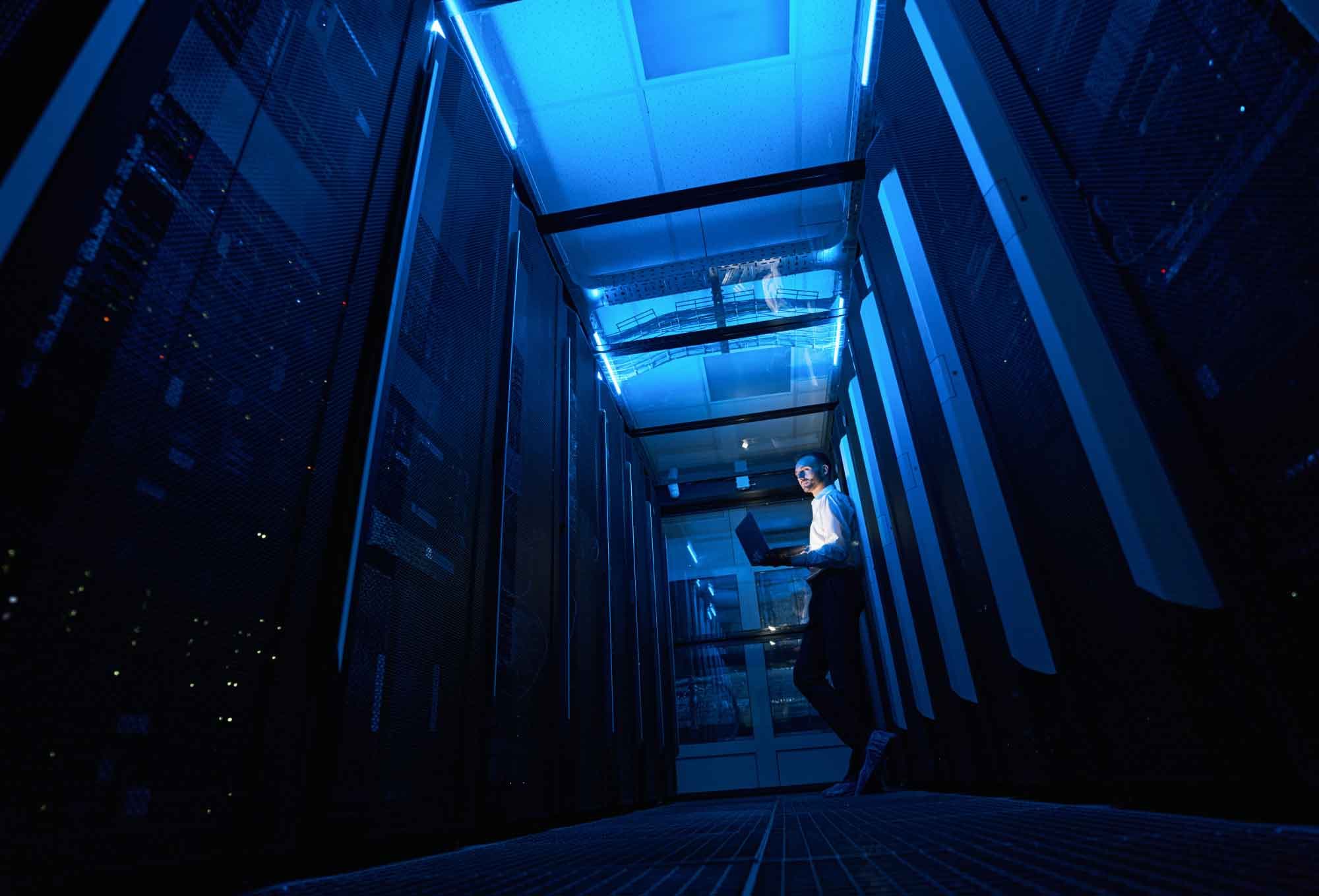 Man standing in a dark server room with ambient blue lighting| Why the break/fix model for IT is dying