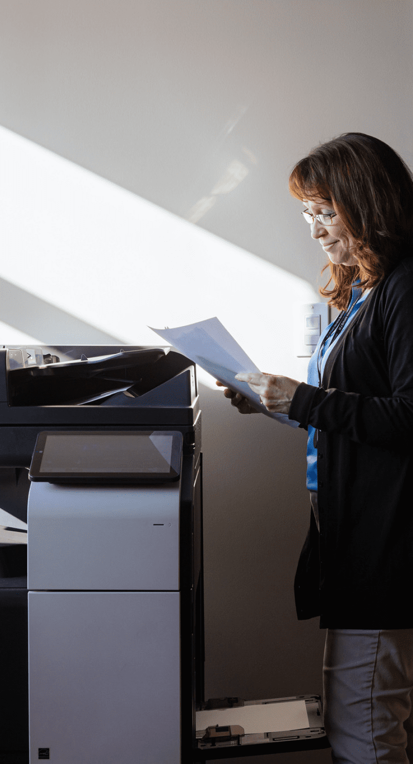 Person holding a piece of paper next to a large printer