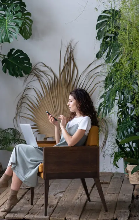 Women working on a laptop in a room with a lot of plants around her.
