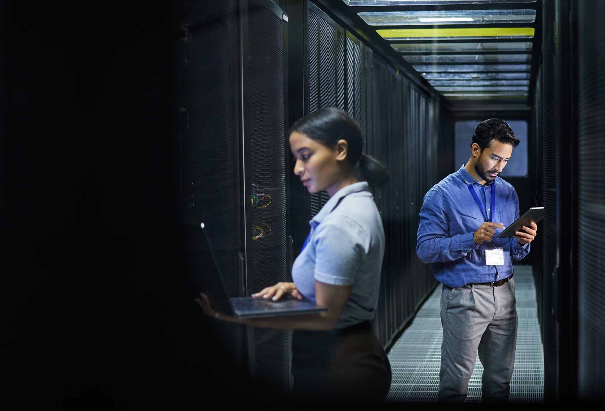 A man and woman working on different devices in a server room