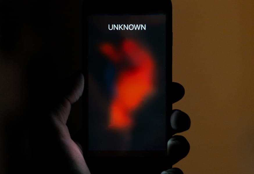 Hand holding smartphone with "unknown" on phone screen and red streak down the screen.